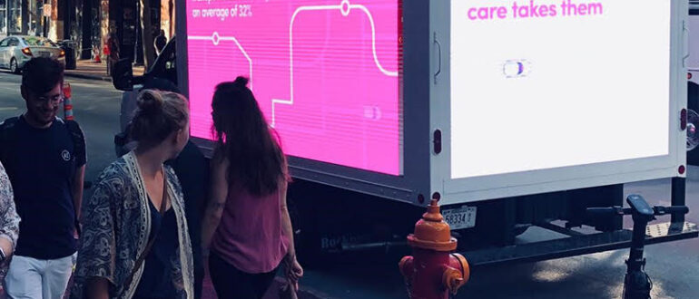 People walking beside a mobile LED billboard displaying vibrant advertisements.